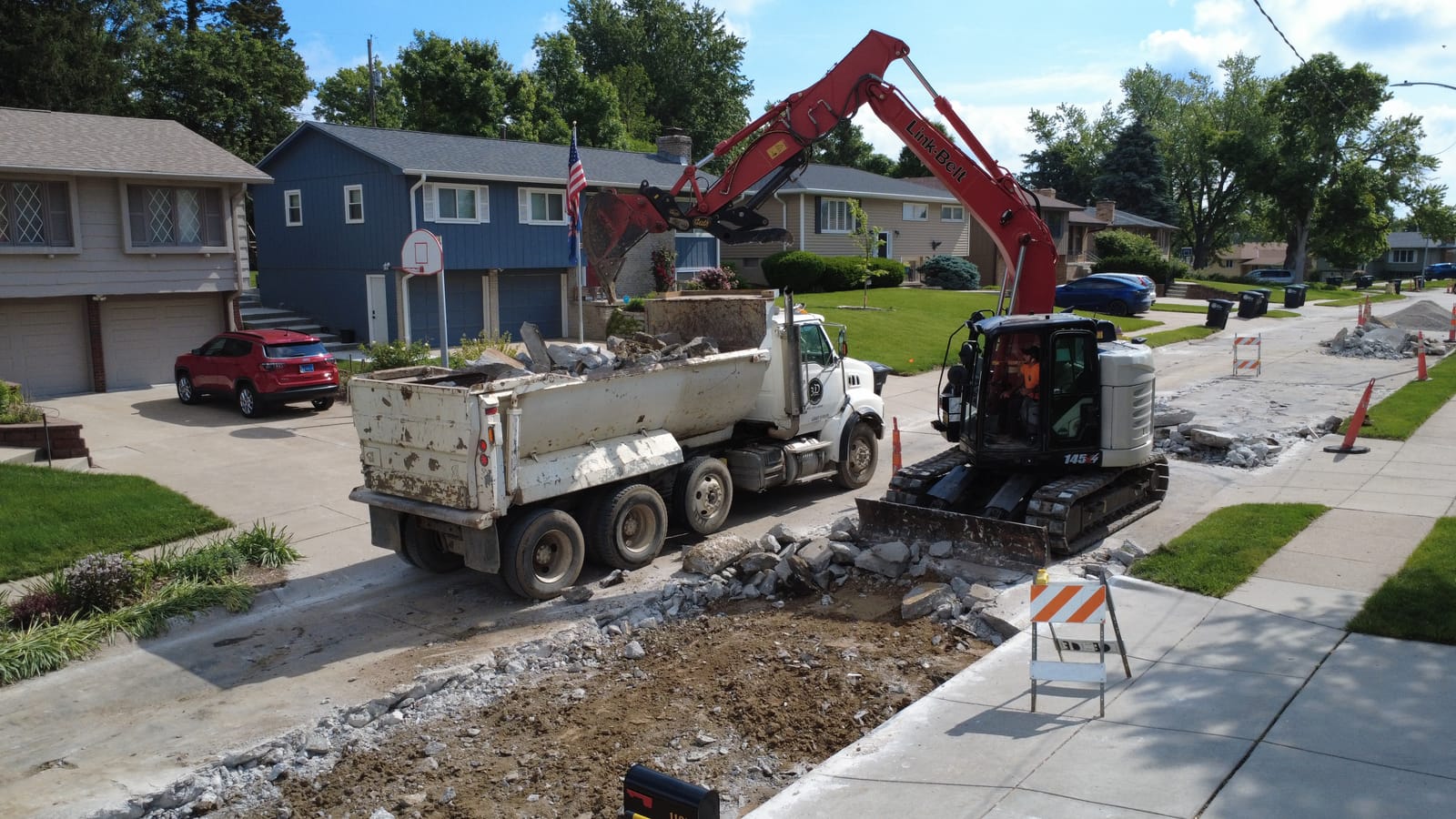 Excavator and dump truck removing concrete on a residential street